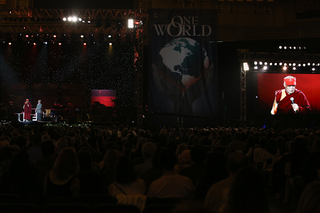 The Dalai Lama speaks to the audience while also appearing on a jumbo screen.