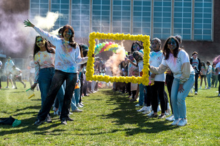 Students line up to wait for a drone to fly through the frame. They prepare their color powder to throw in front of the drone as it passes by.